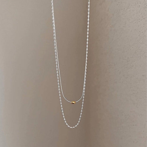 Minimalistische gelaagde zilveren sieraden ketting met gouden boon-accent, met rijstkralen patroon, ideaal voor een trendy mode-accessoire.