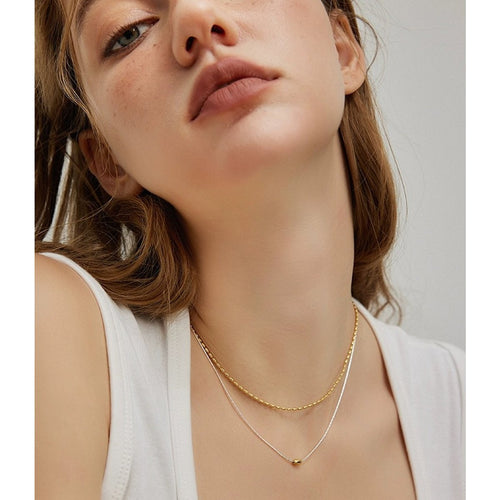 Elegante tweevoudige zilveren ketting met gouden boon-accent, minimalistisch ontwerp met rijstkralen patroon, perfect voor moderne mode.